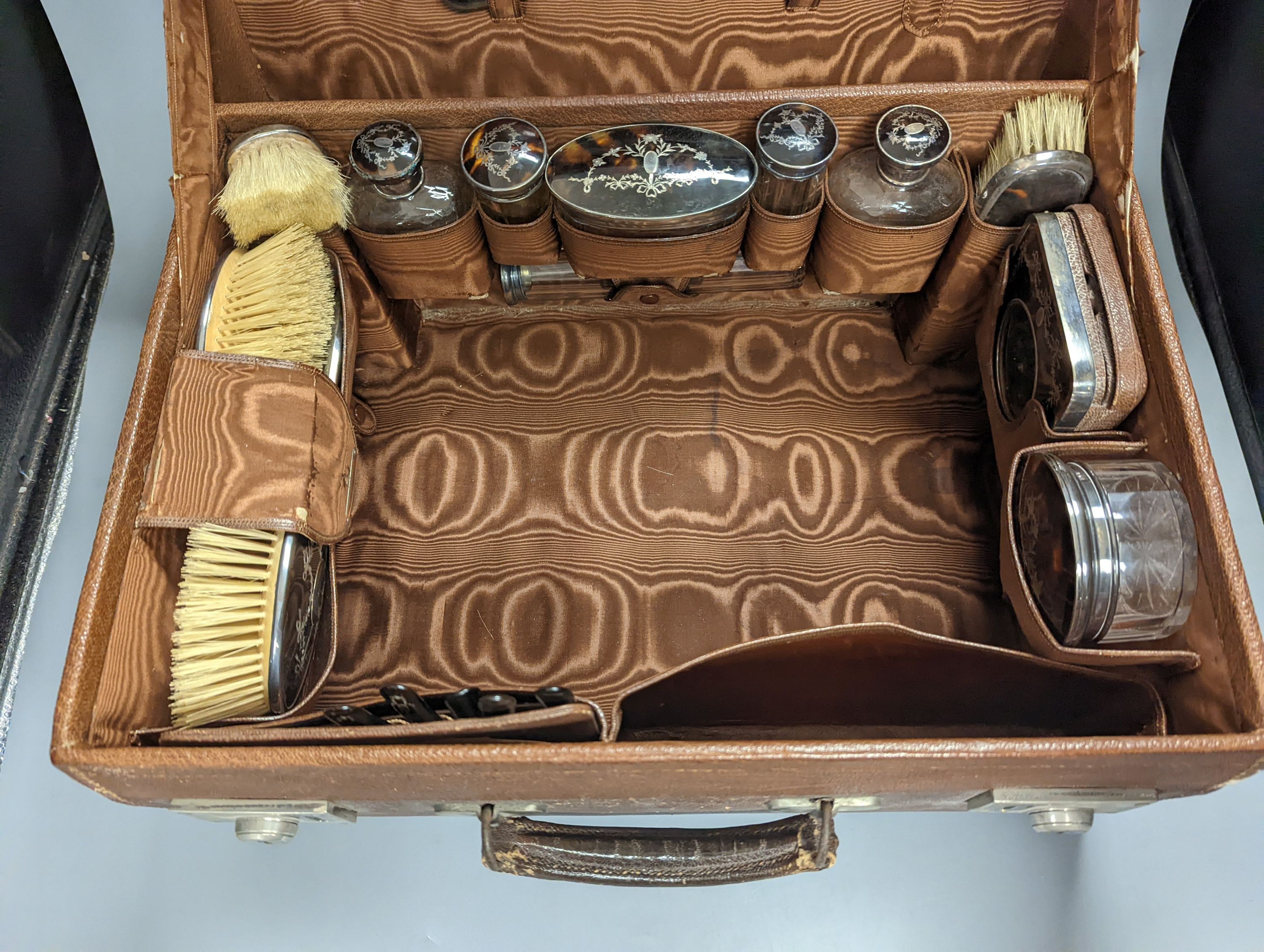 A George V leather travelling toilet case, containing twenty one matched, mainly silver and tortoiseshell pique items including toilet jars, brushes, mirror and pocket watch holder, mostly Levi & Salaman, Birmingham, 191